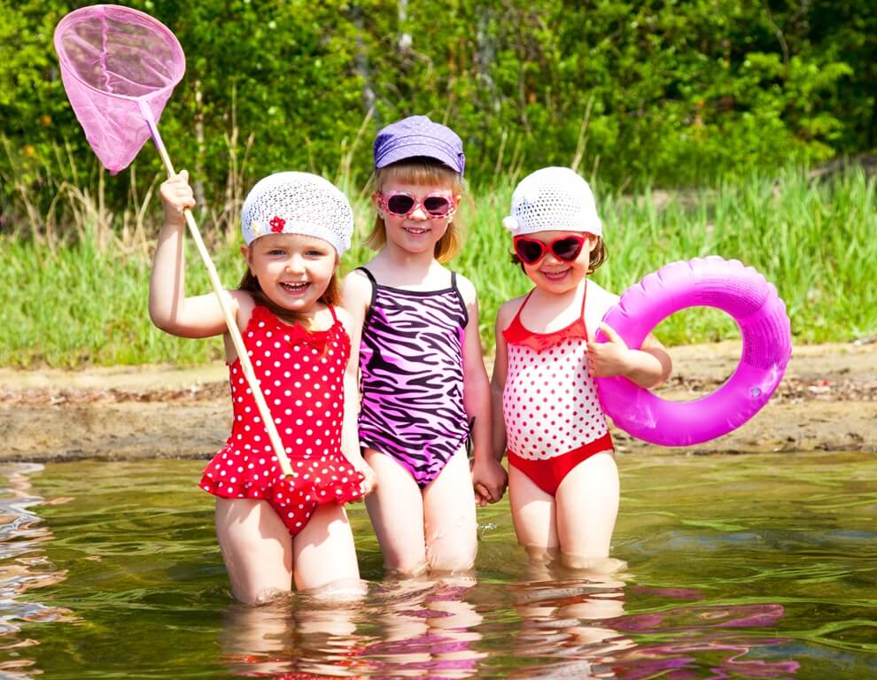 Photo of three happy little girls in bathing suits, up to their knees in the lake.